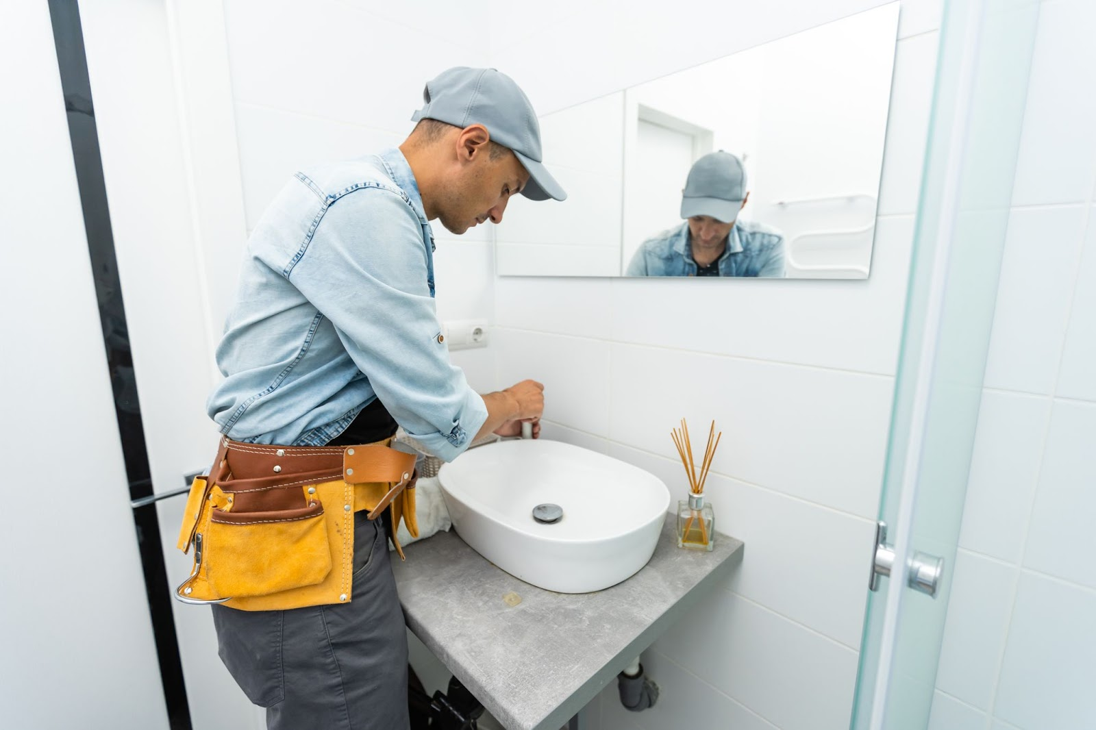 Plumber with yellow tool belt installs new bathroom sink