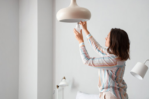 A woman replacing a light bulb in a home.