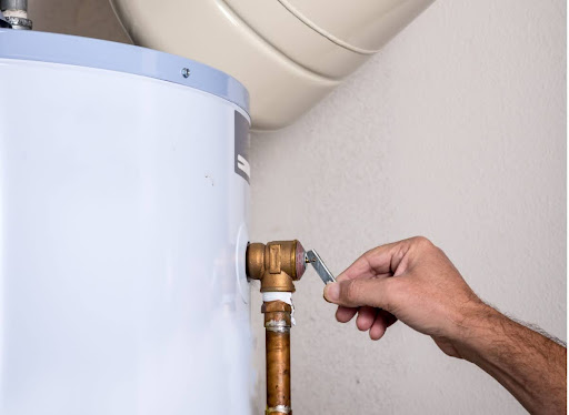 A hand reaching up to adjust a water heater's pressure relief valve.