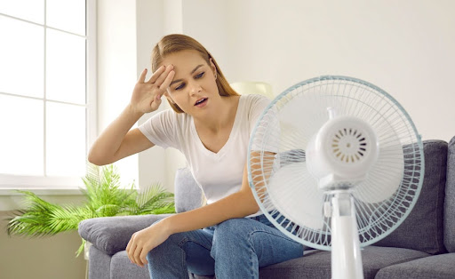 A woman sitting on a couch in front of a fan.