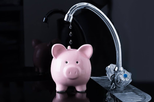 A faucet dripping into a piggy bank.