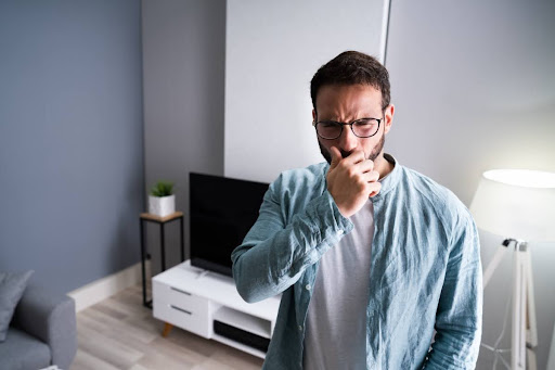 A man reaching up to cover his nose due to a bad smell in his home.