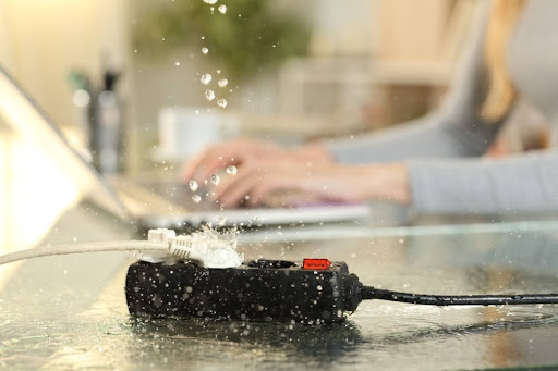 A woman using a laptop while water hits an extension cord in the foreground, creating an electrical hazard.