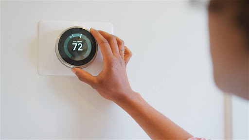 A person adjusting a smart thermostat. The thermostat's screen reads "cool set to 72."