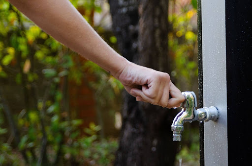 A person turning the handle on an outdoor faucet.