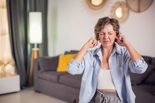 A woman in a living room covering her ears due to a loud noise.